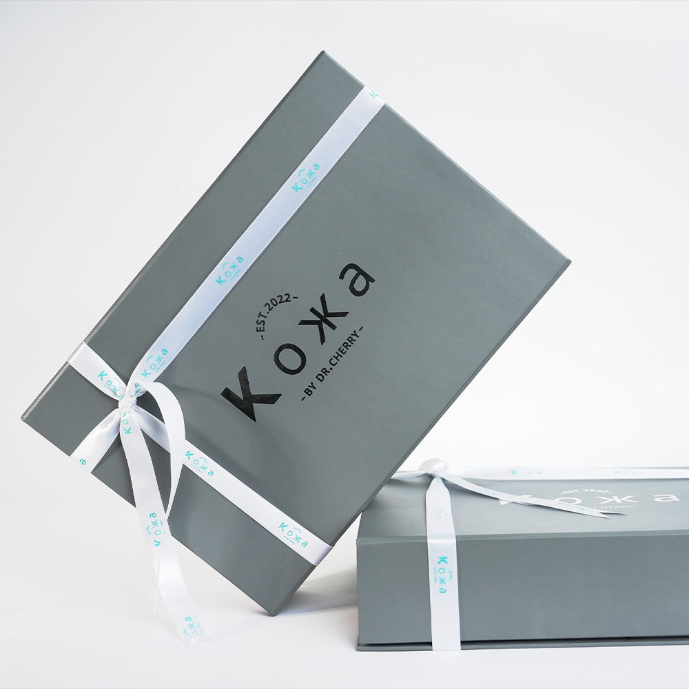 Gray gift box with white ribbon and 'Koxa' branding on a light gray background